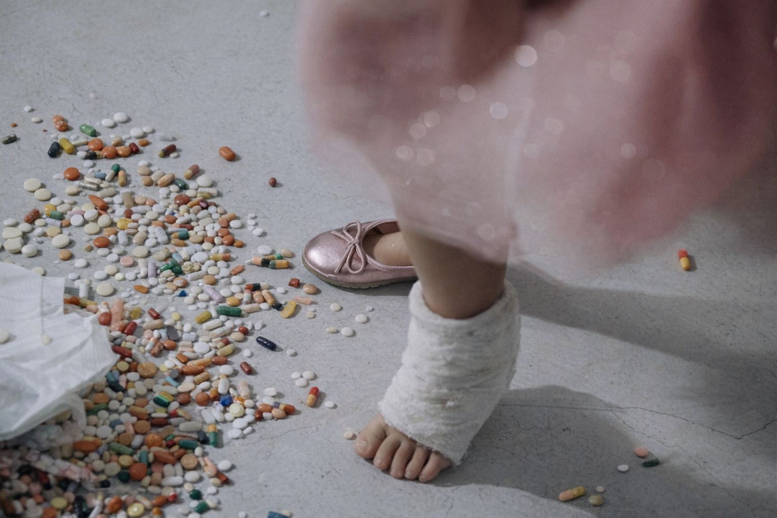 Pieds d'enfant près d'un tapis de pilules colorées au sol.